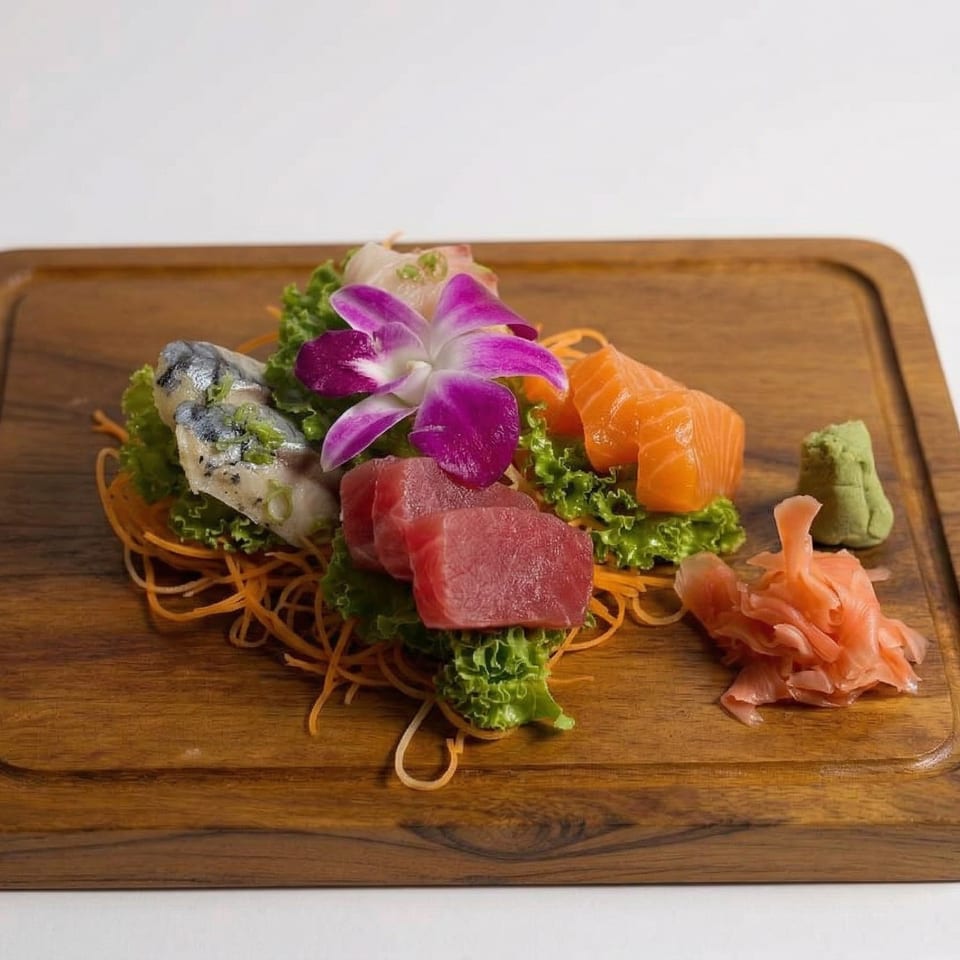 Sashimi platter with tuna, salmon, and mackerel, garnished with a purple orchid, ginger, and wasabi.